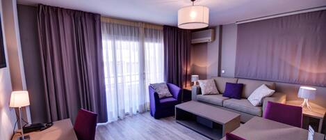 A modern hotel room with a sofa, armchair, and a dining table.