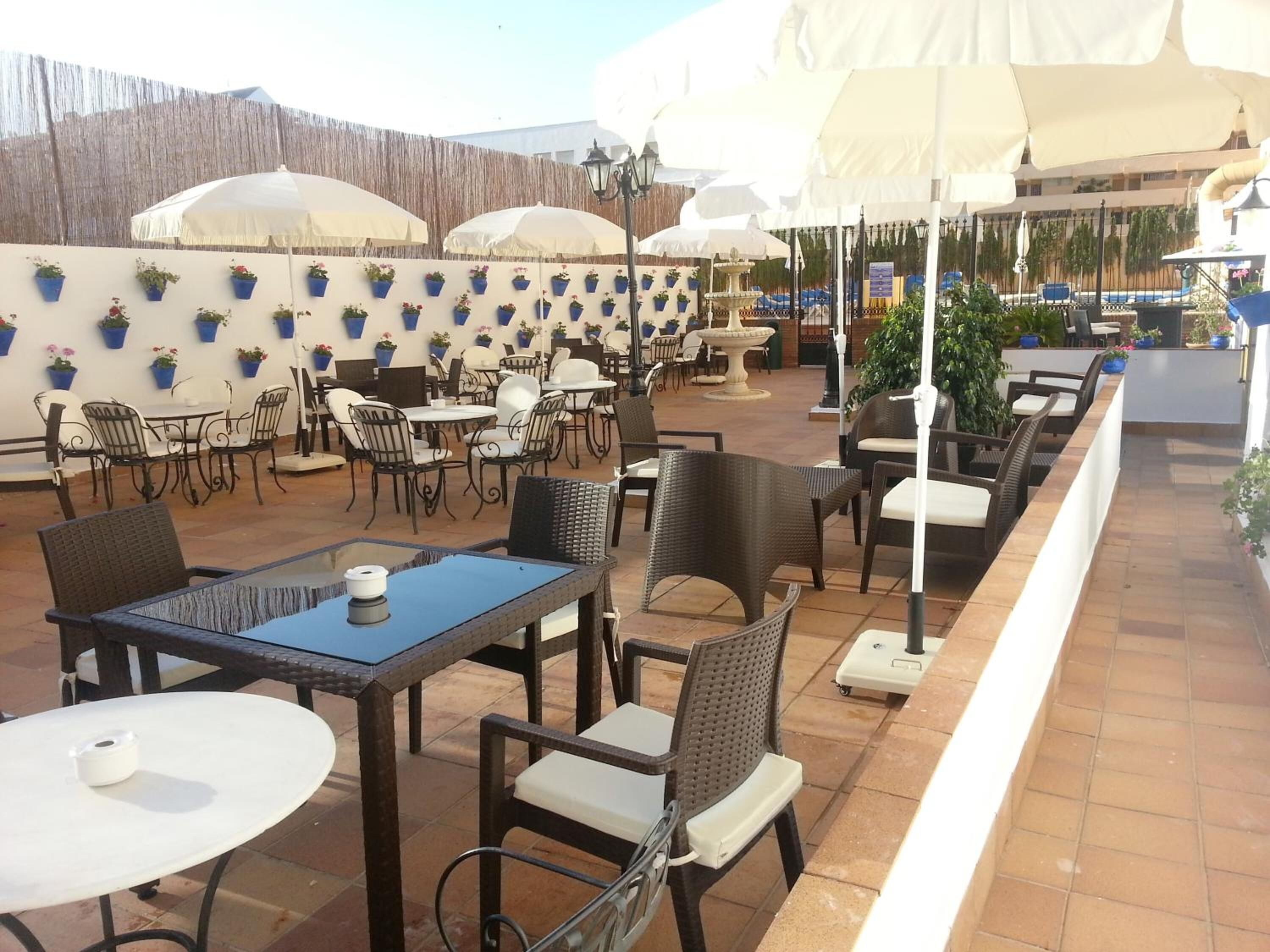 Un espace extérieur aménagé en terrasse, avec des tables et des chaises, des parasols et des plantes en pot.