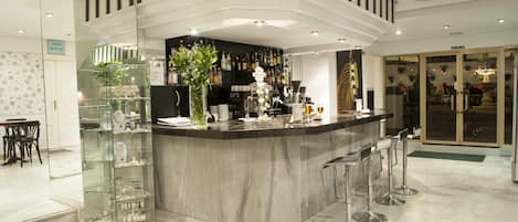 Un área de bar moderna con una barra de mármol, vitrinas de vidrio y una zona de estar con taburetes.