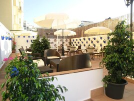 Een buitenterras met wicker meubels, parasols en potplanten.