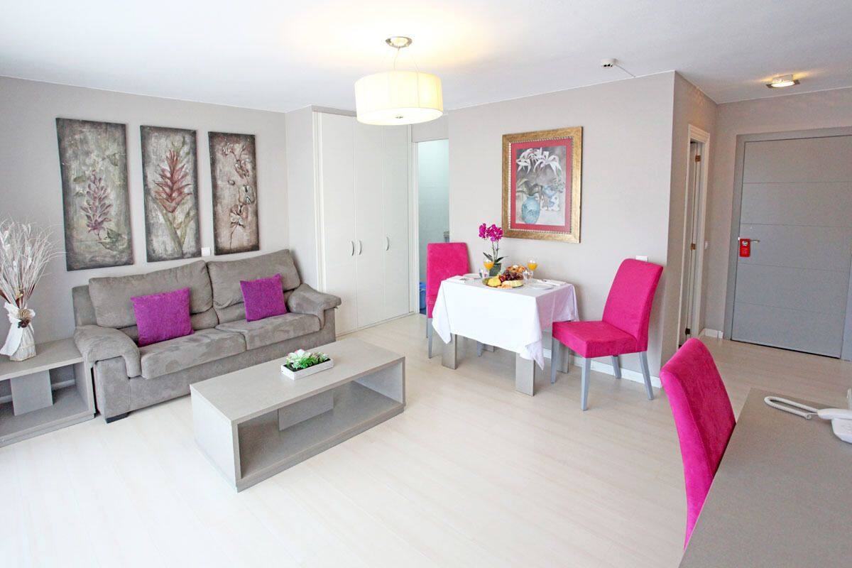 A modern living room with a grey sofa, a coffee table, a dining table with pink chairs, and artwork on the walls.