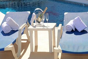 Een zwembadterras met twee ligbedden, een tafel met champagne, twee glazen en een handdoek op elk bed.