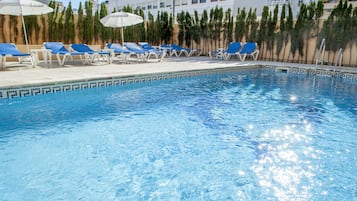 Une piscine à l’eau bleue, entourée de chaises longues et de parasols.