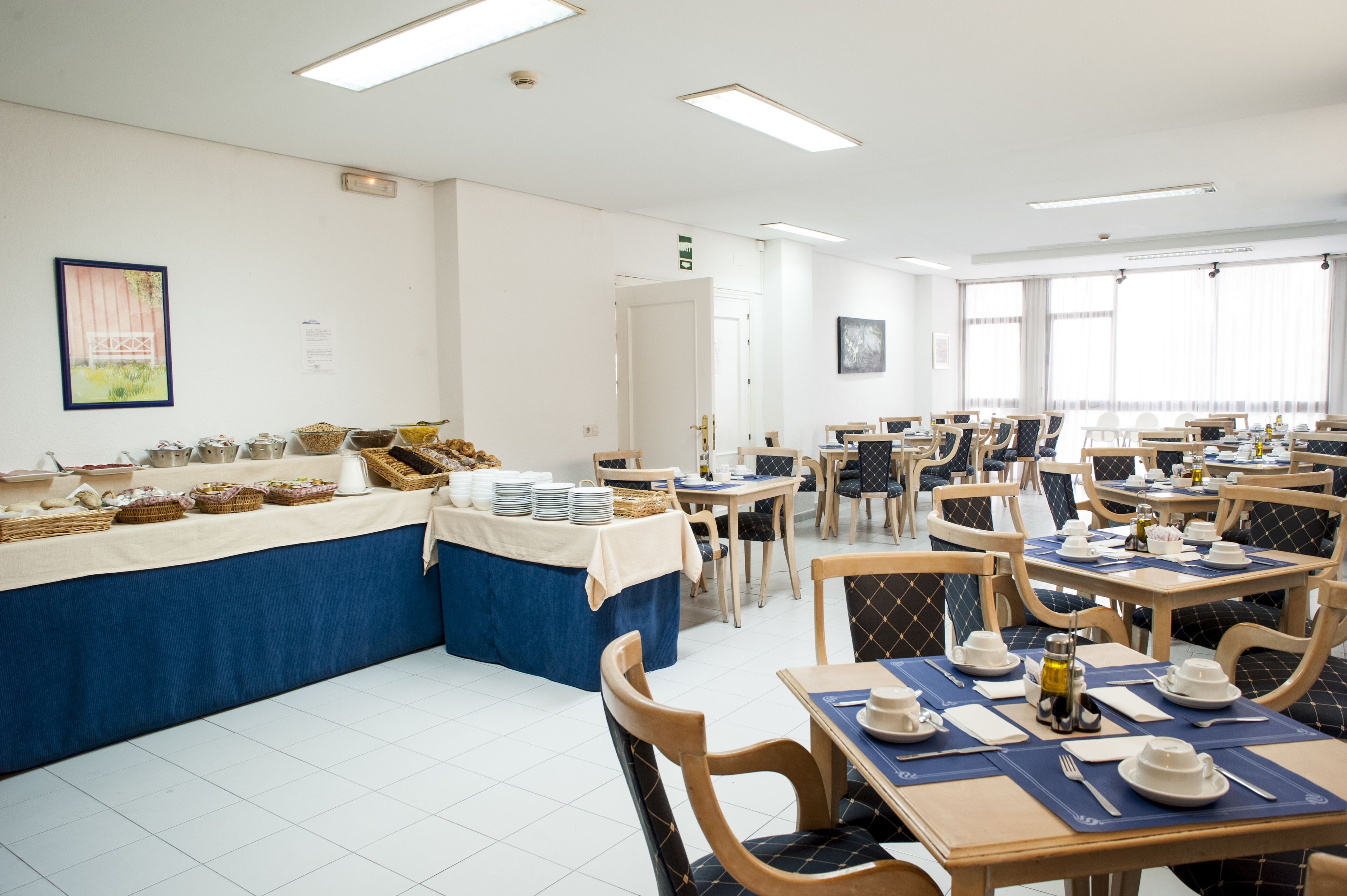 A dining area with tables set for breakfast, featuring baskets of bread and pastries.