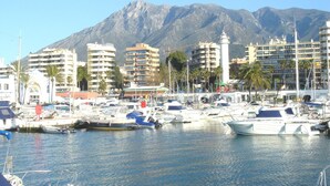 A marina with boats docked, surrounded by buildings and mountains in the background. - Hotel El Faro Marbella (Marbella)
