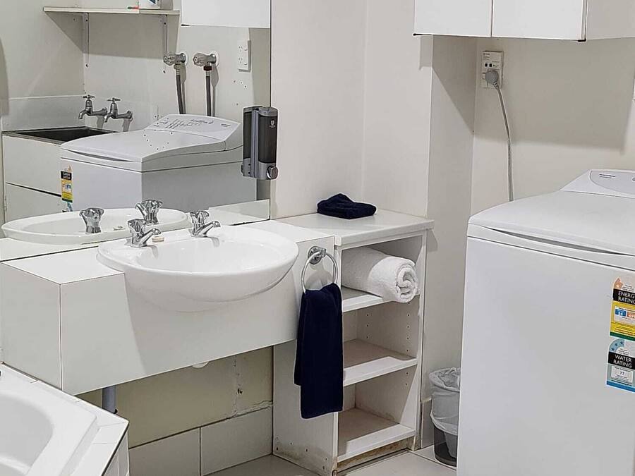 A small, clean bathroom with white fixtures, a sink, a toilet, and a mirror. There are two towel racks and a small shelf.