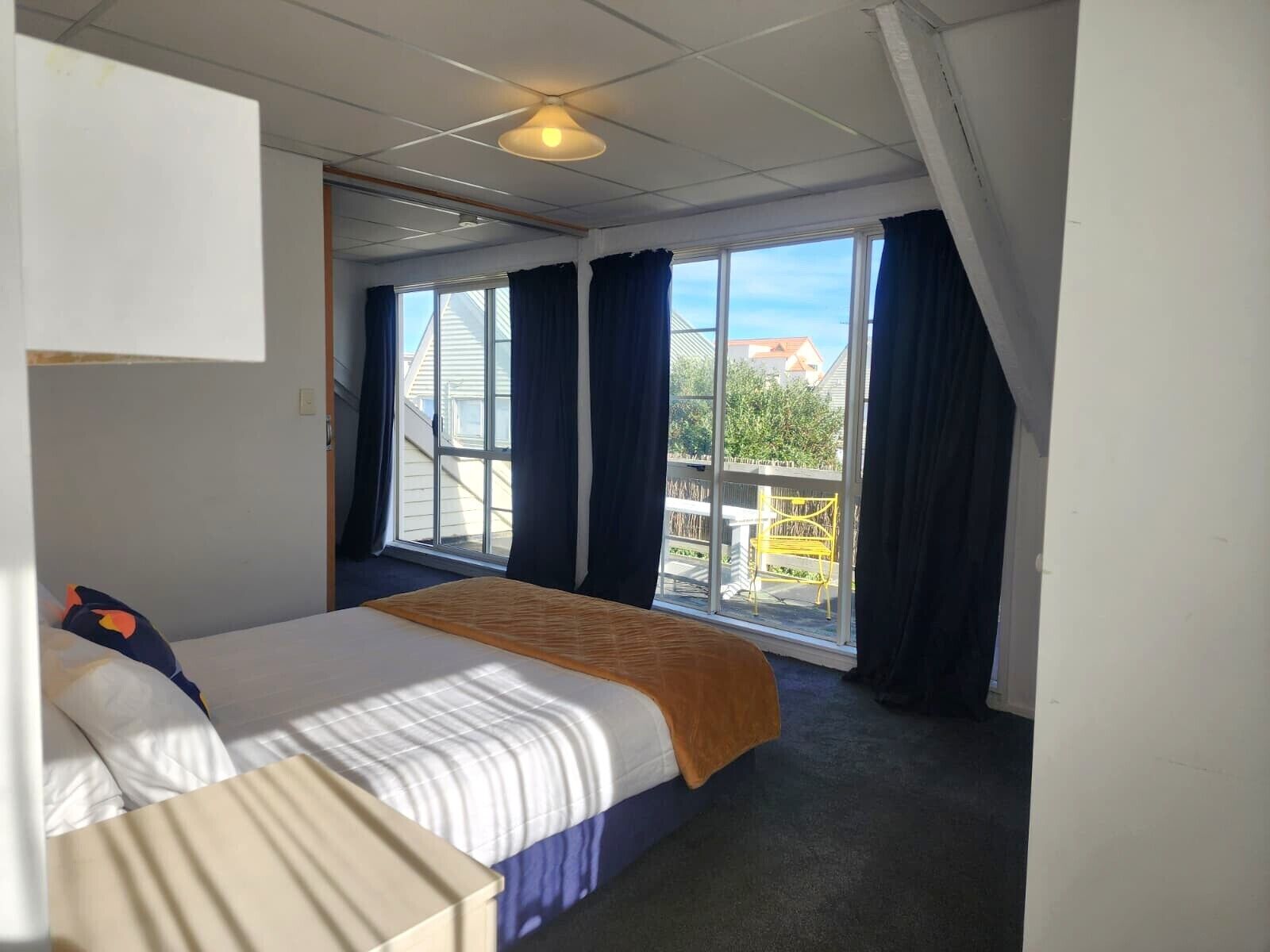 A hotel room with a bed, a window with curtains, and a view of the outside.