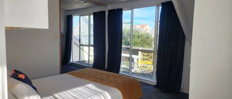 A hotel room with a bed, a window with curtains, and a view of the outside.
