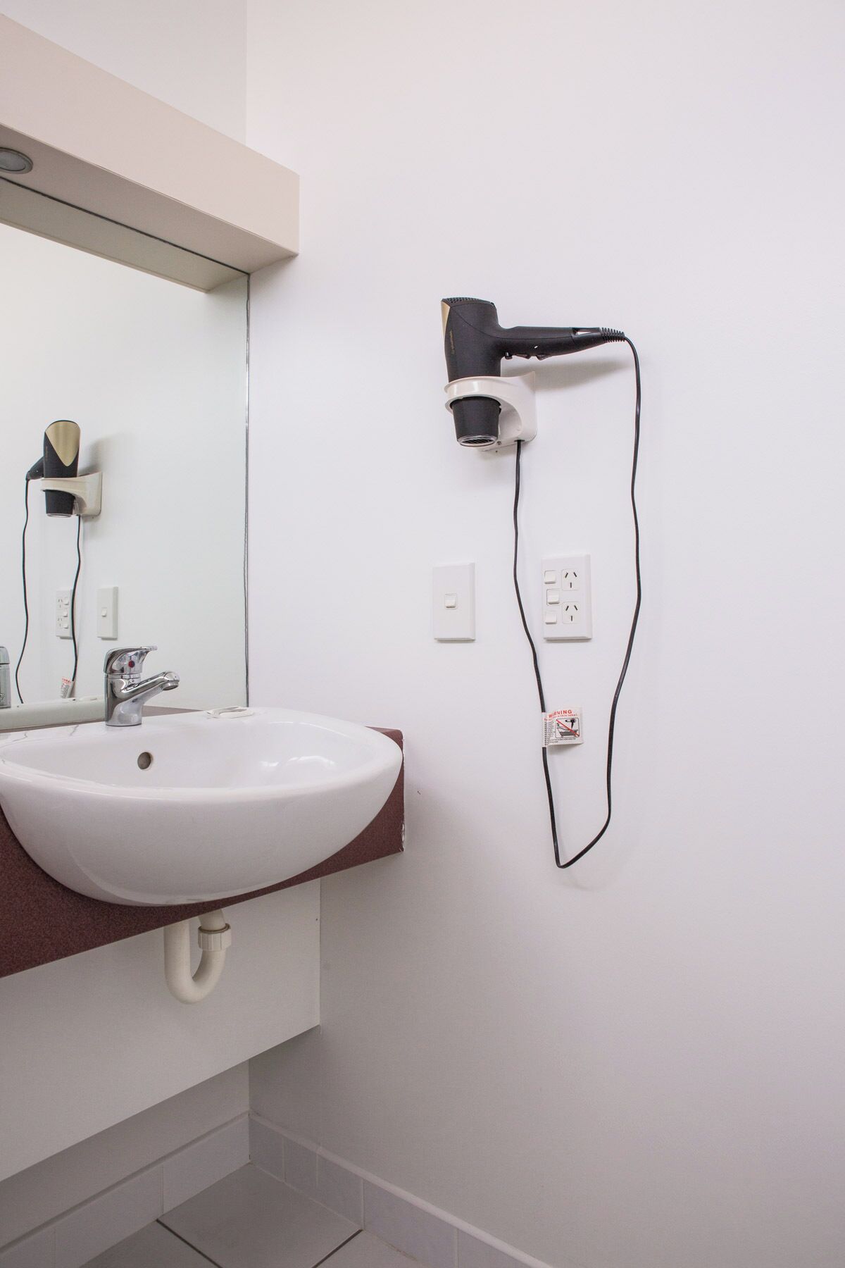 Un baño con lavamanos blanco, un espejo y un secador de pelo montado en la pared.