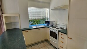 A kitchen with a black countertop, white cabinets, a stove, and a window with blinds. -  U Studios Paraparaumu, SureStay Collection by BW (Paraparaumu)