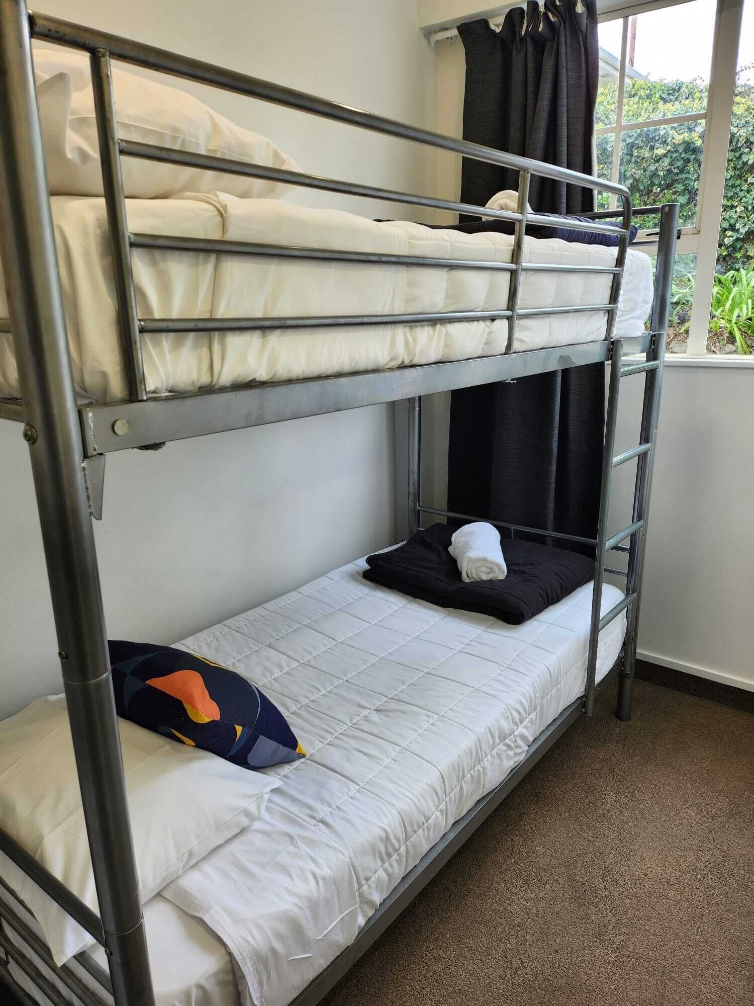 A bunk bed with white bedding, a black pillow, and a colorful pillow on the lower bunk.