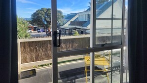 A view from inside a room through a window, featuring a street with parked cars, a building with a sloped roof, and a wooden fence. -  U Studios Paraparaumu, SureStay Collection by BW (Paraparaumu)