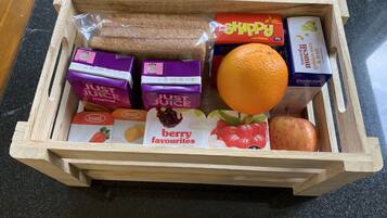 Una cassa di legno contenente diversi alimenti, tra cui cereali in scatola, succo di frutta, pane tostato e un'arancia intera.