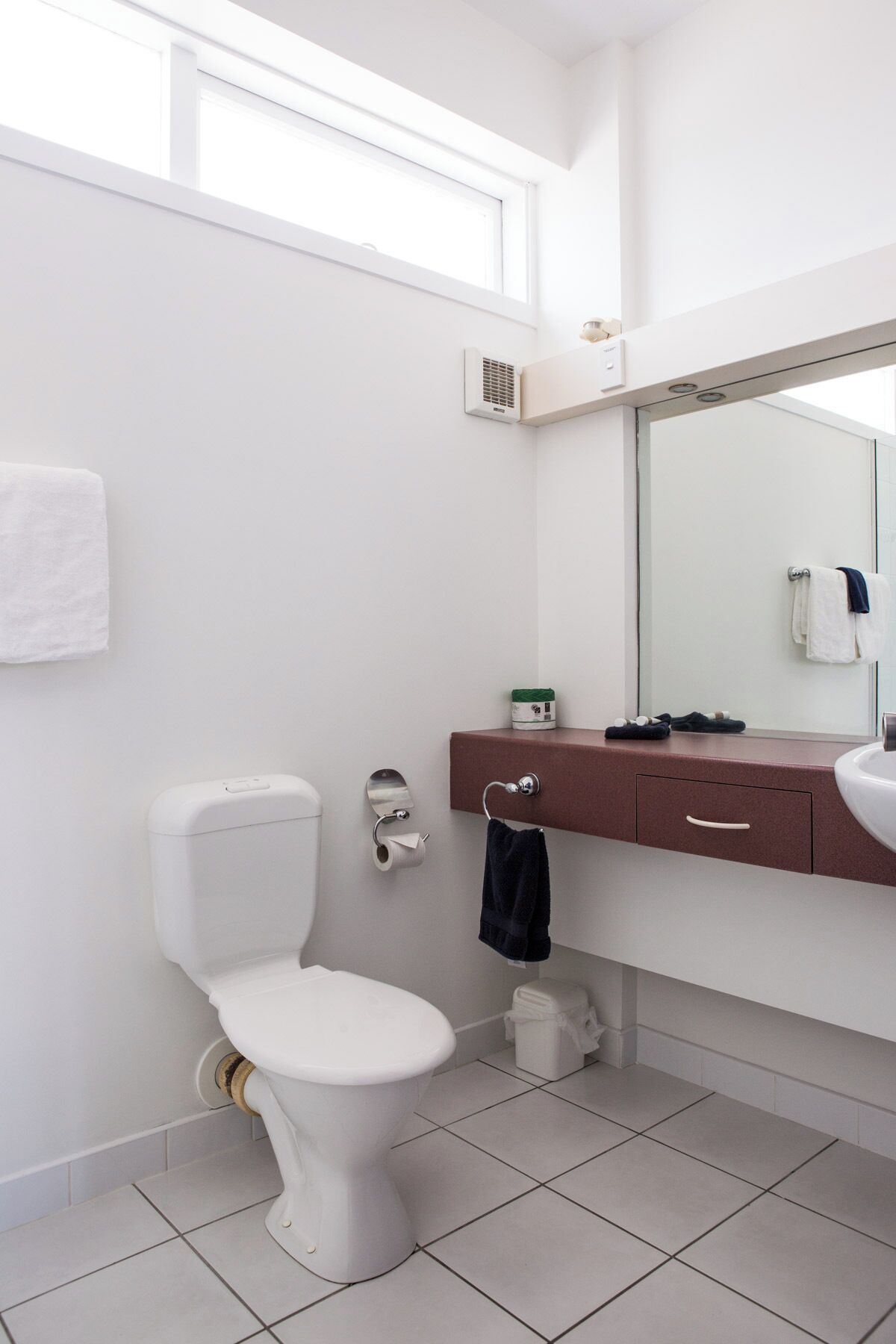 A modern bathroom with a white toilet, a vanity with a mirror, and a window above the sink.