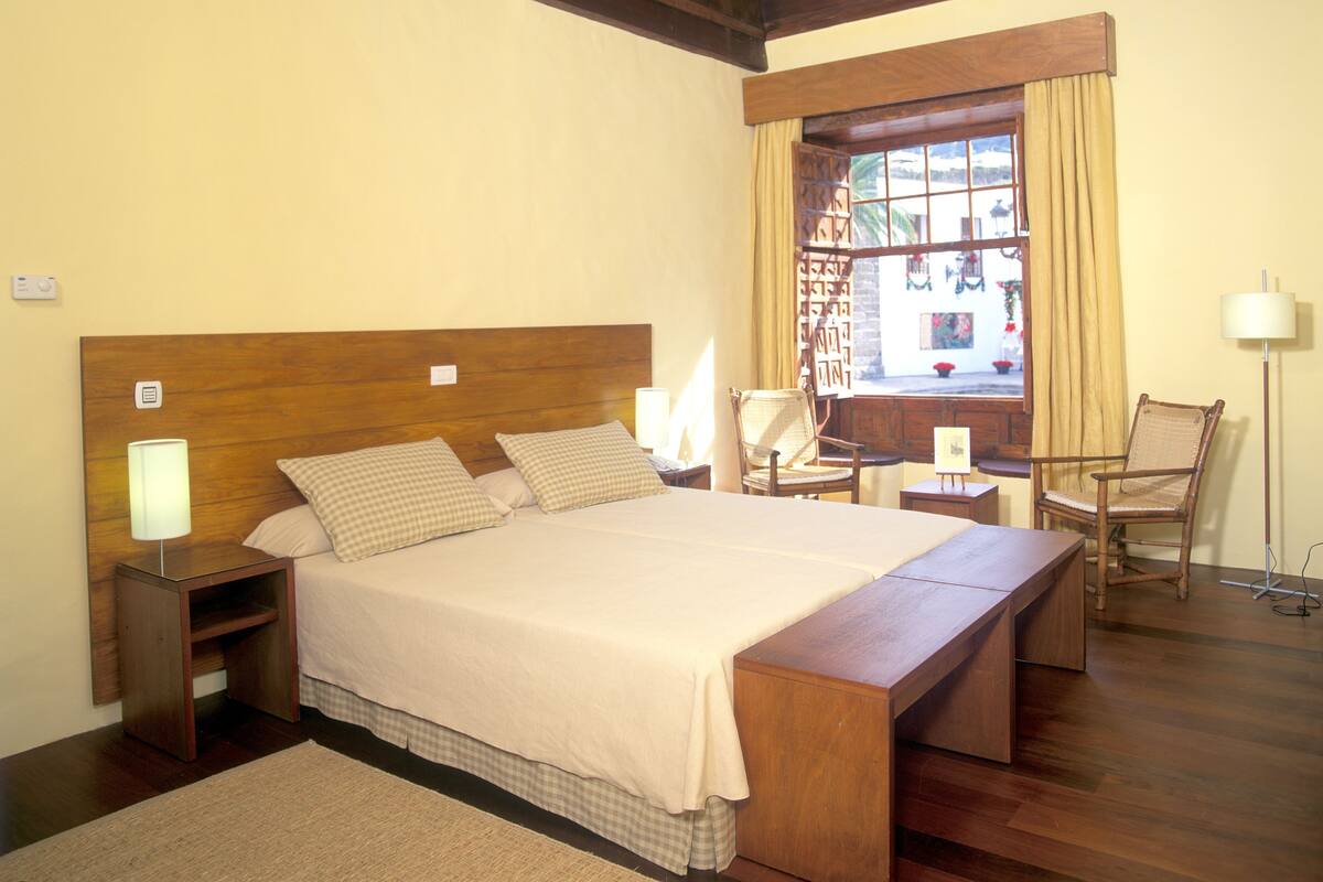 A bedroom with a wooden bed, bedside tables, a chair, a desk, and a window with curtains.