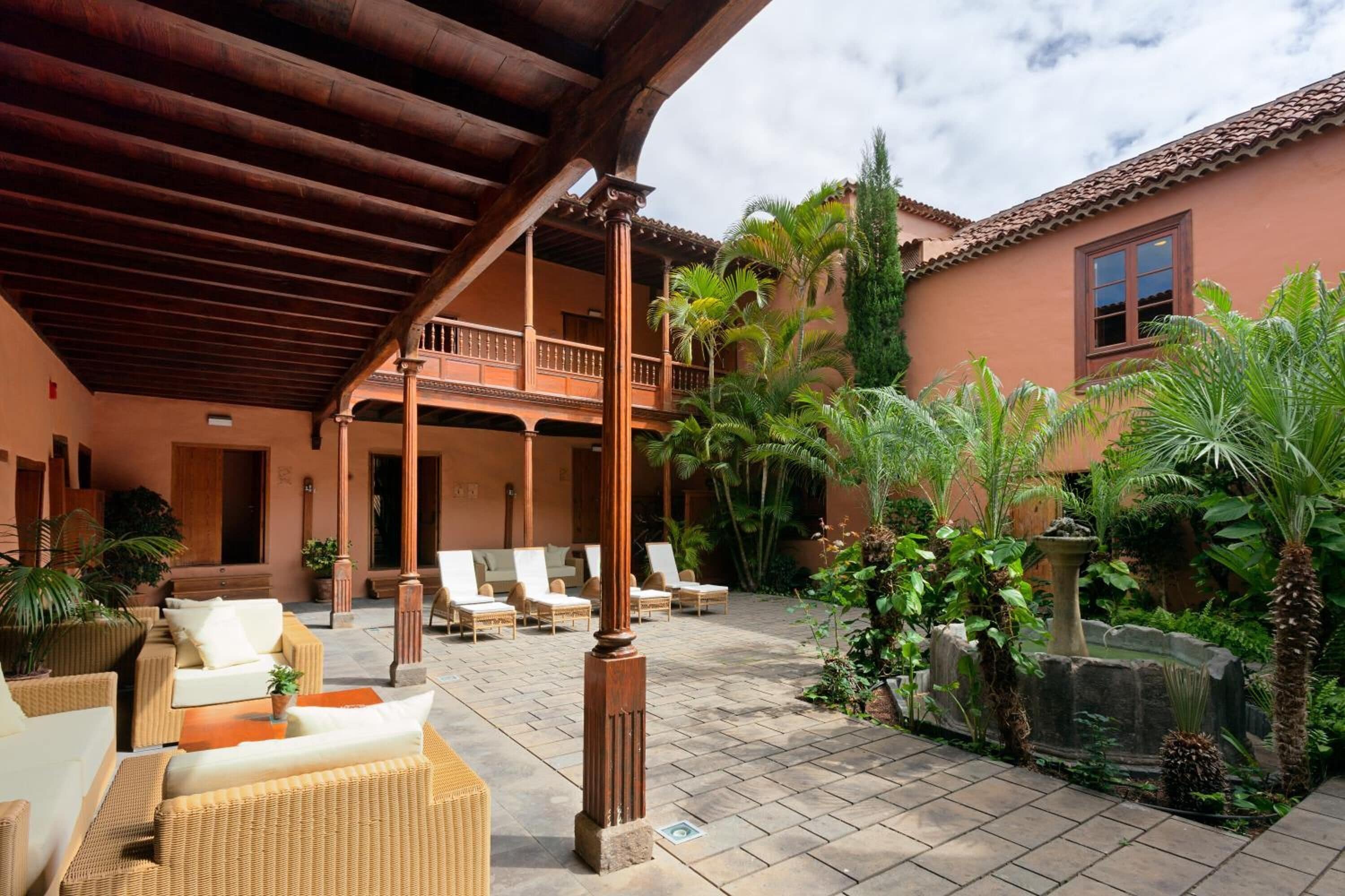 A covered outdoor area with wicker furniture, a fountain, and lush greenery.