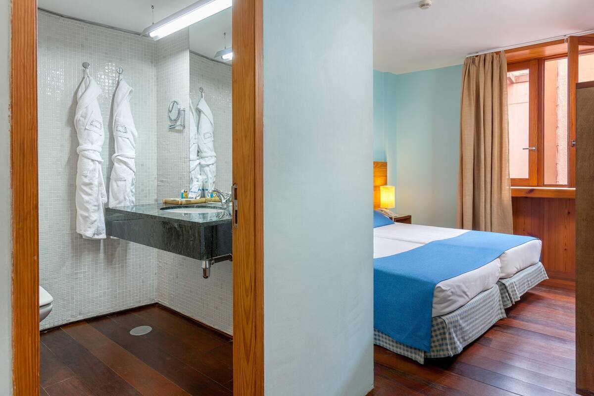 A bathroom with a tiled wall, a sink, and two white towels hanging on hooks.
