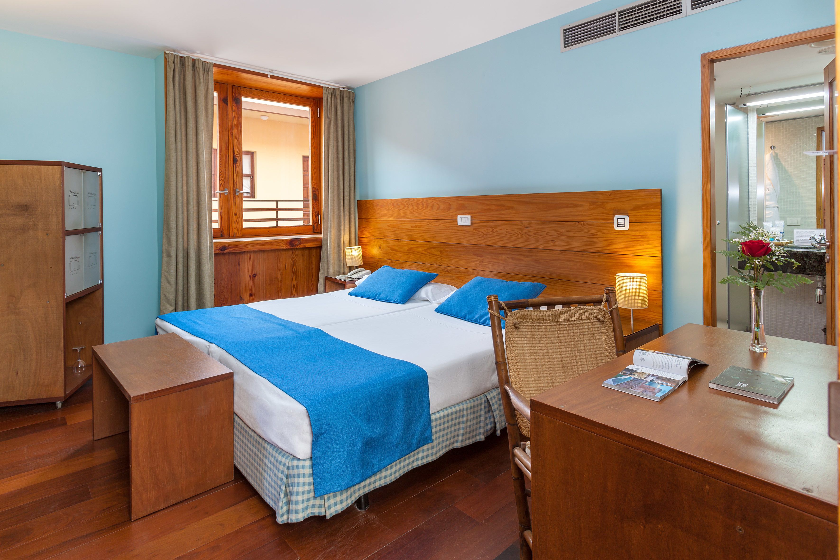Une chambre d’hôtel avec un grand lit, une tête de lit en bois, un bureau avec une chaise, une petite table et un miroir.