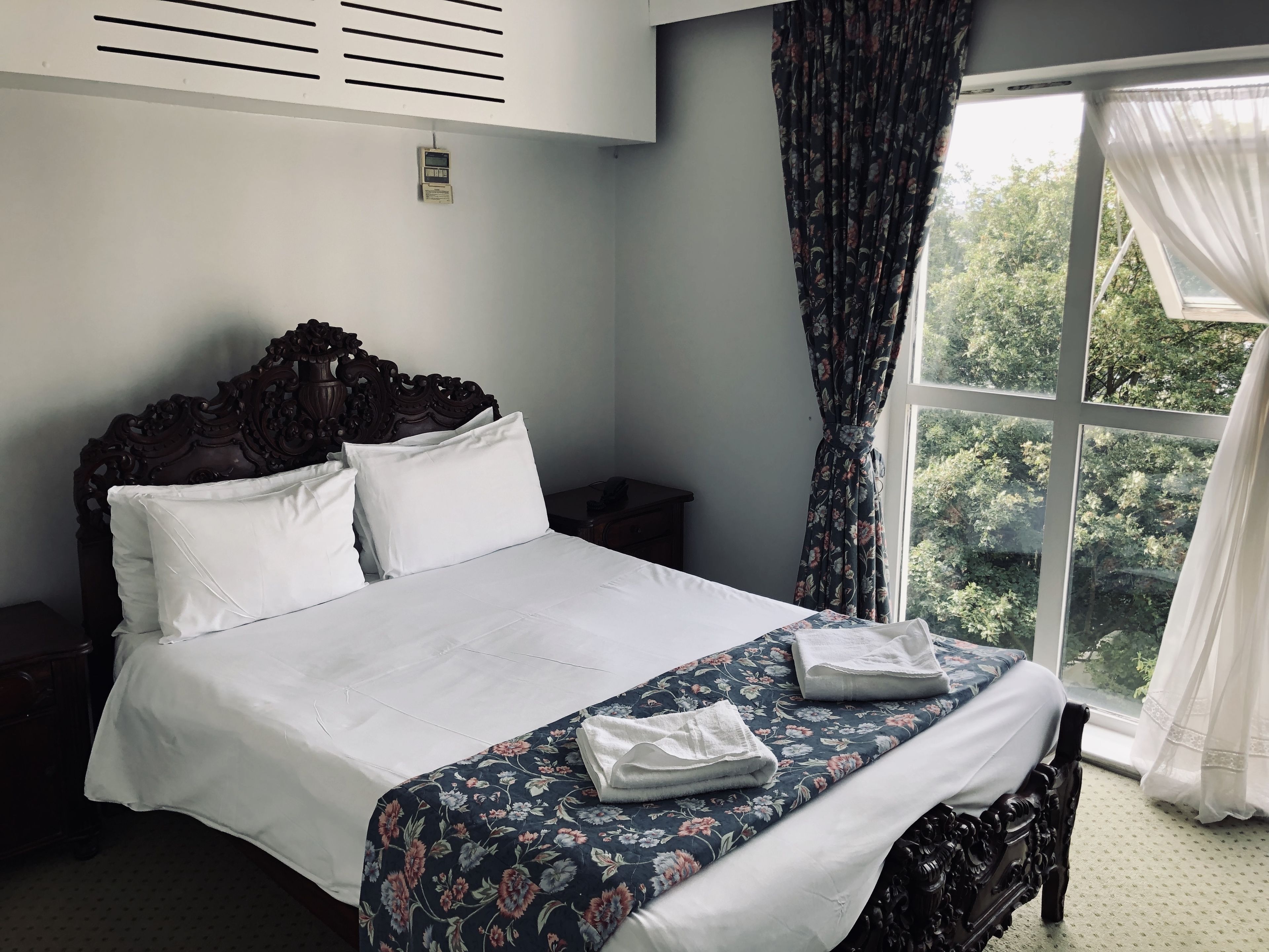 A neatly made bed with a floral bedspread, a wooden headboard, and white pillows.