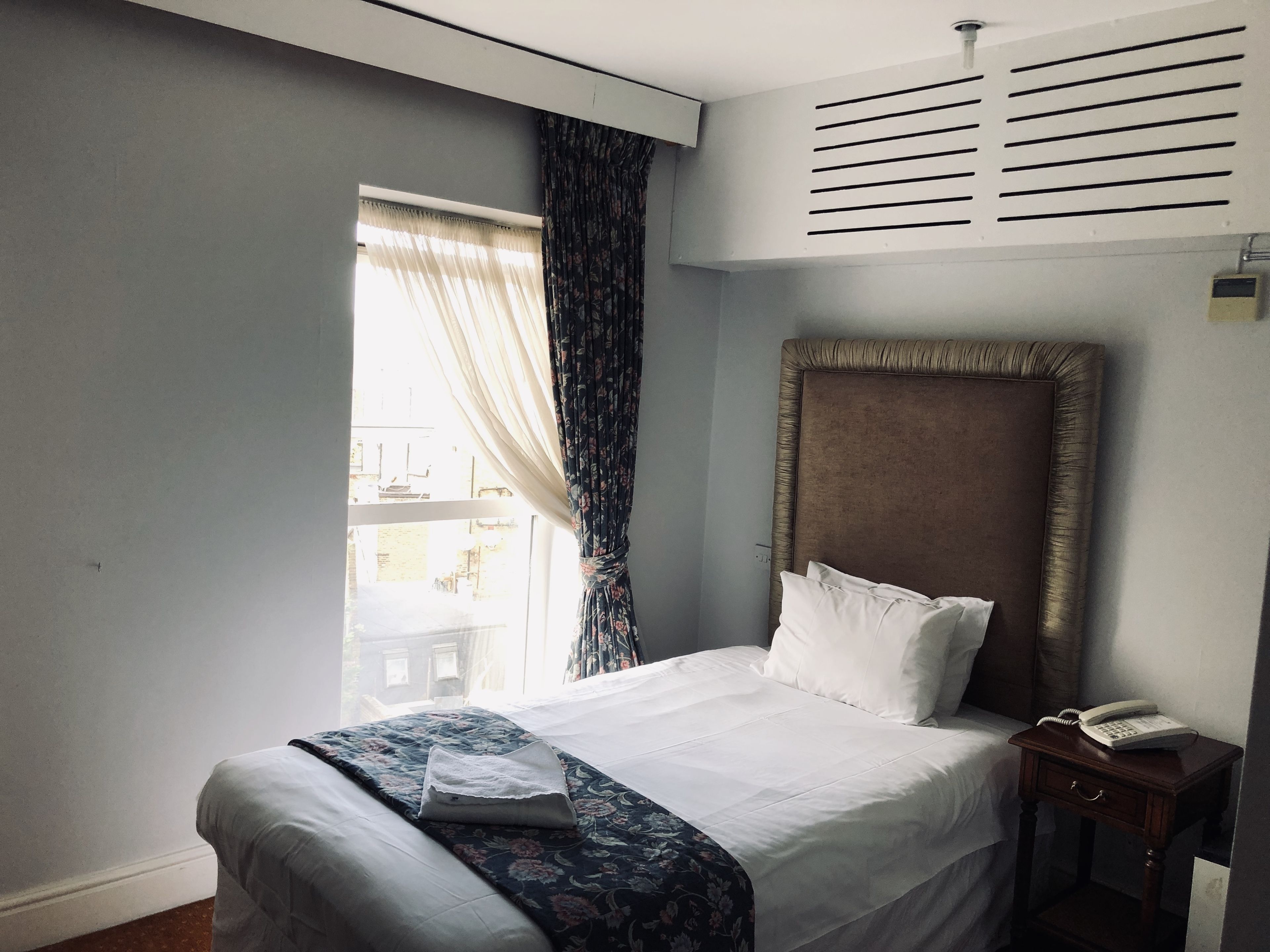 A hotel room with a large bed, a bedside table with a telephone, and a window with curtains.