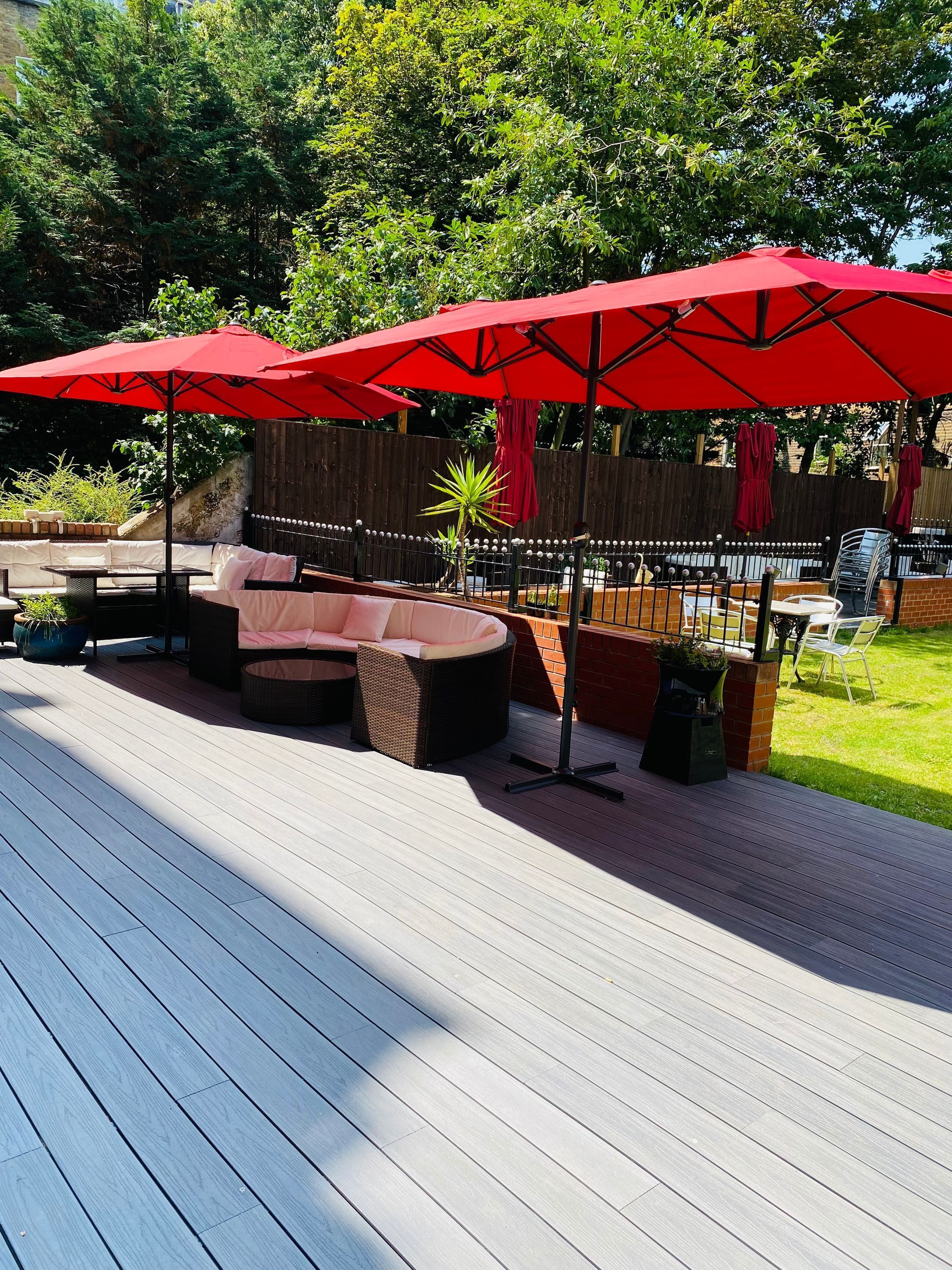 A deck with outdoor furniture, including a sofa and chairs, under red umbrellas.