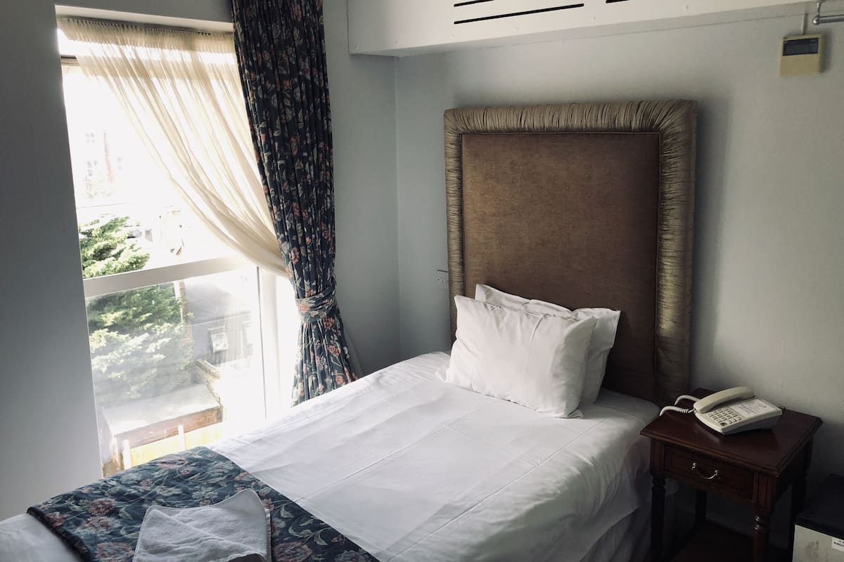 Una camera d'albergo con un letto, un comodino con il telefono e una finestra con tende.