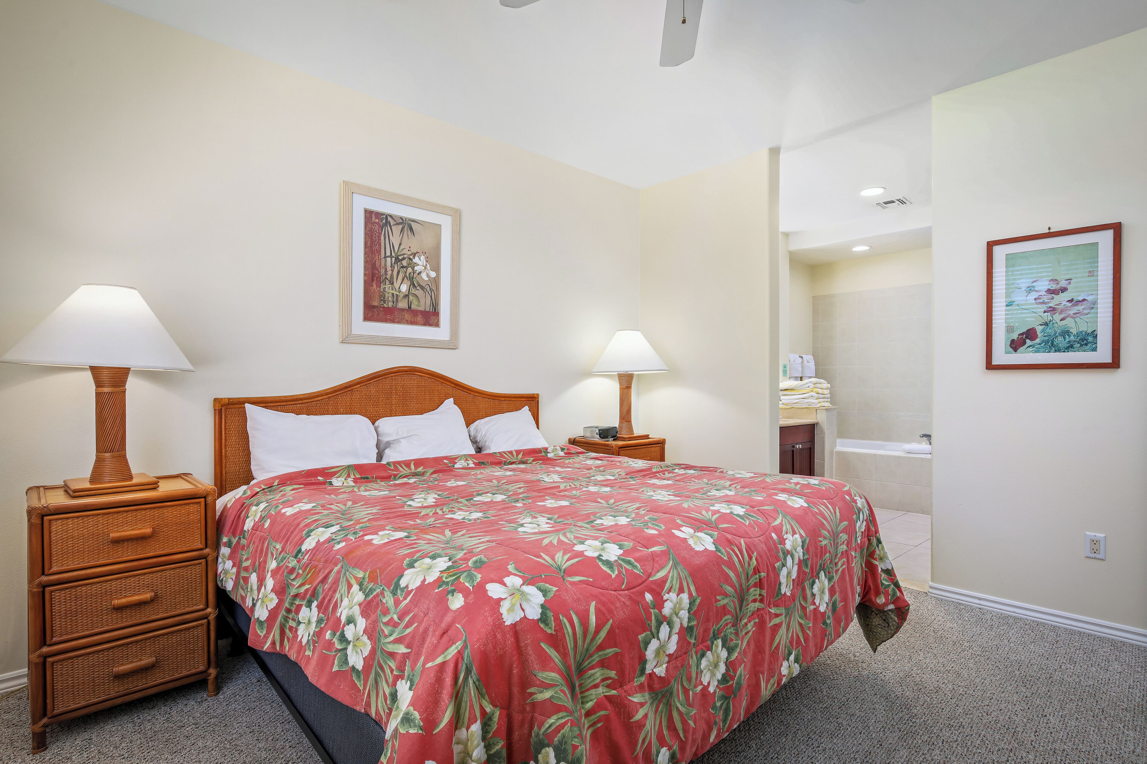Habitación de hotel con una cama, dos mesitas de noche con lámparas, una mesita auxiliar y un baño con bañera, además de dos cuadros en las paredes.