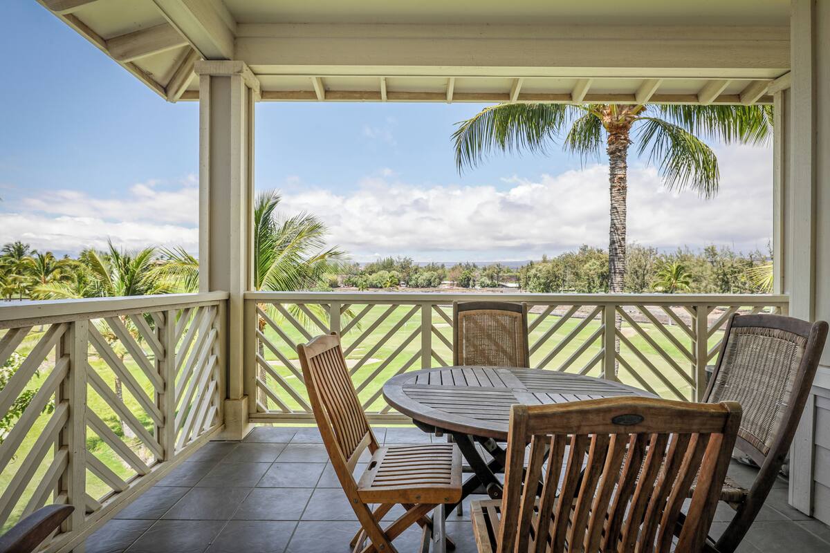 Une terrasse extérieure couverte, avec une table et des chaises, donnant sur un jardin aménagé et agrémentée d’un palmier.