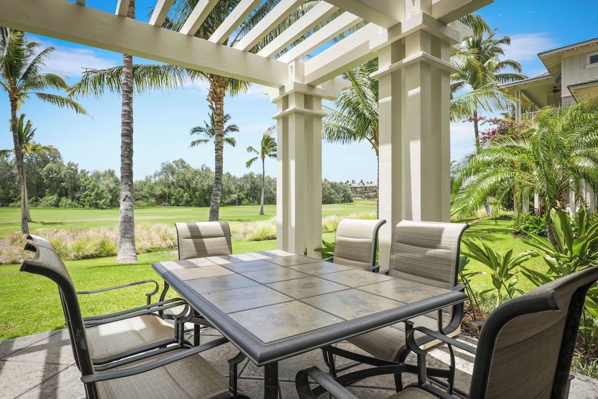Une terrasse extérieure avec une table et des chaises, entourée de palmiers et offrant une vue sur un terrain de golf.