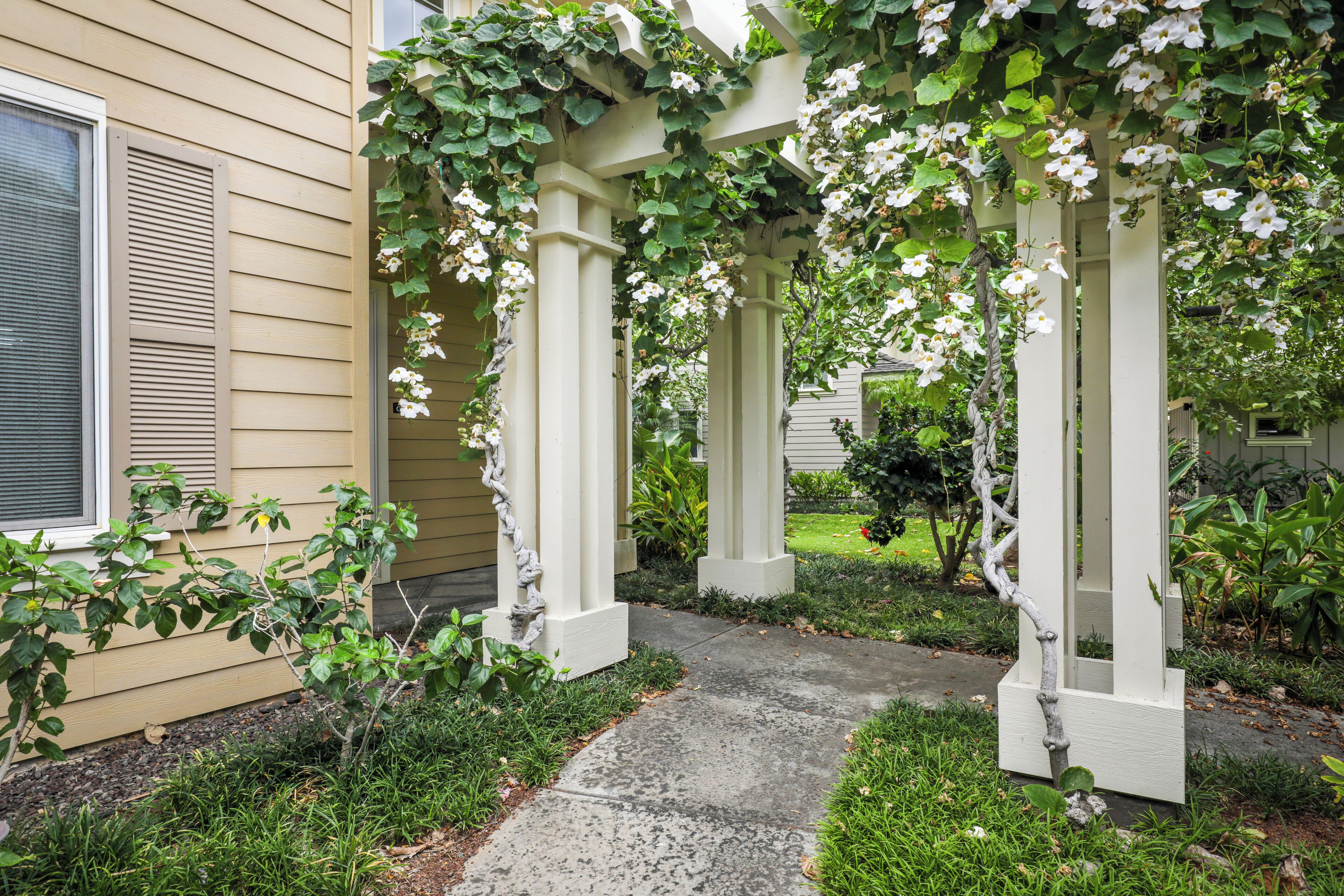 En havegang, der fører hen til en hvid pergola med slyngplanter og blomster.