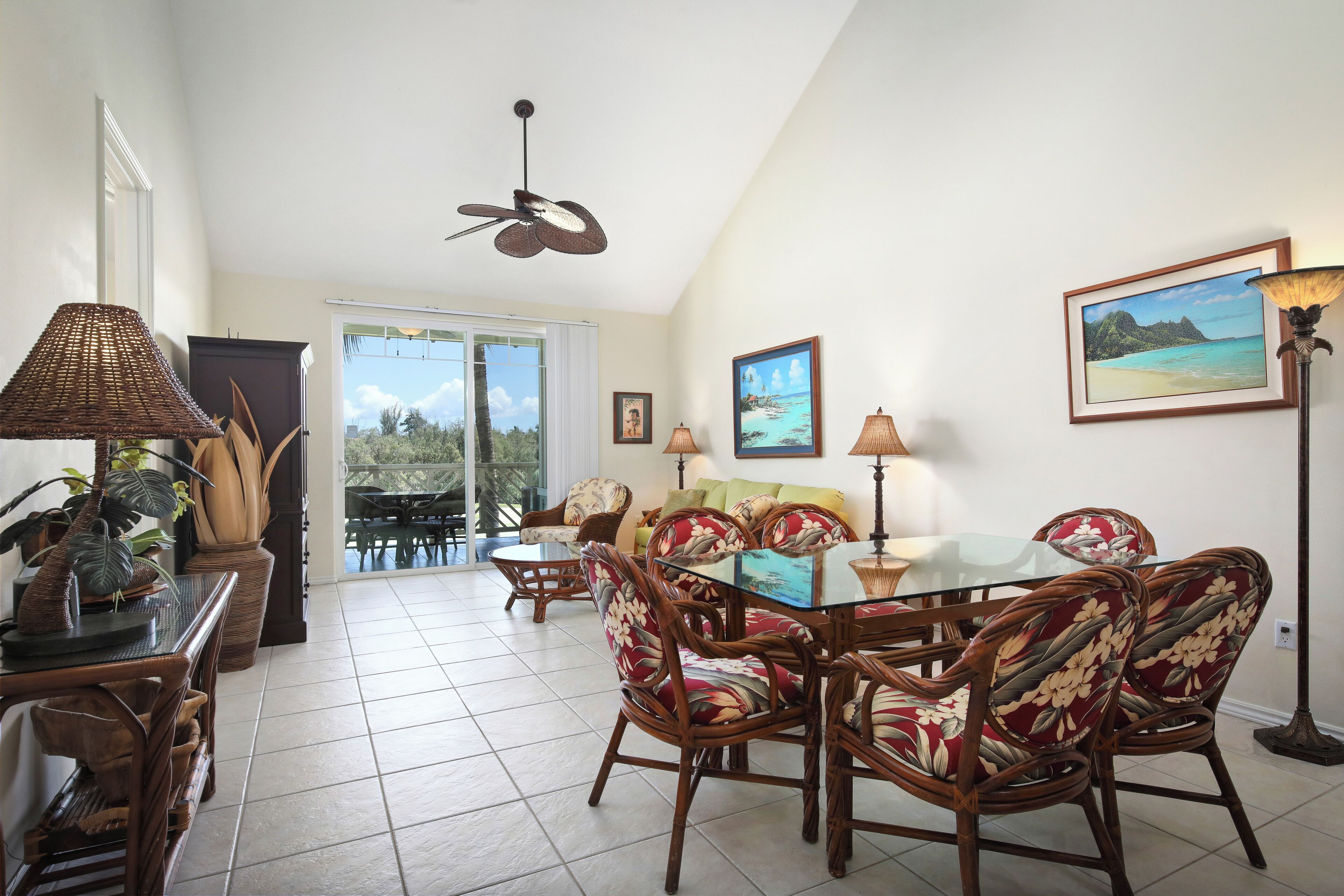 A dining area with wicker chairs, a glass table, and a ceiling fan.