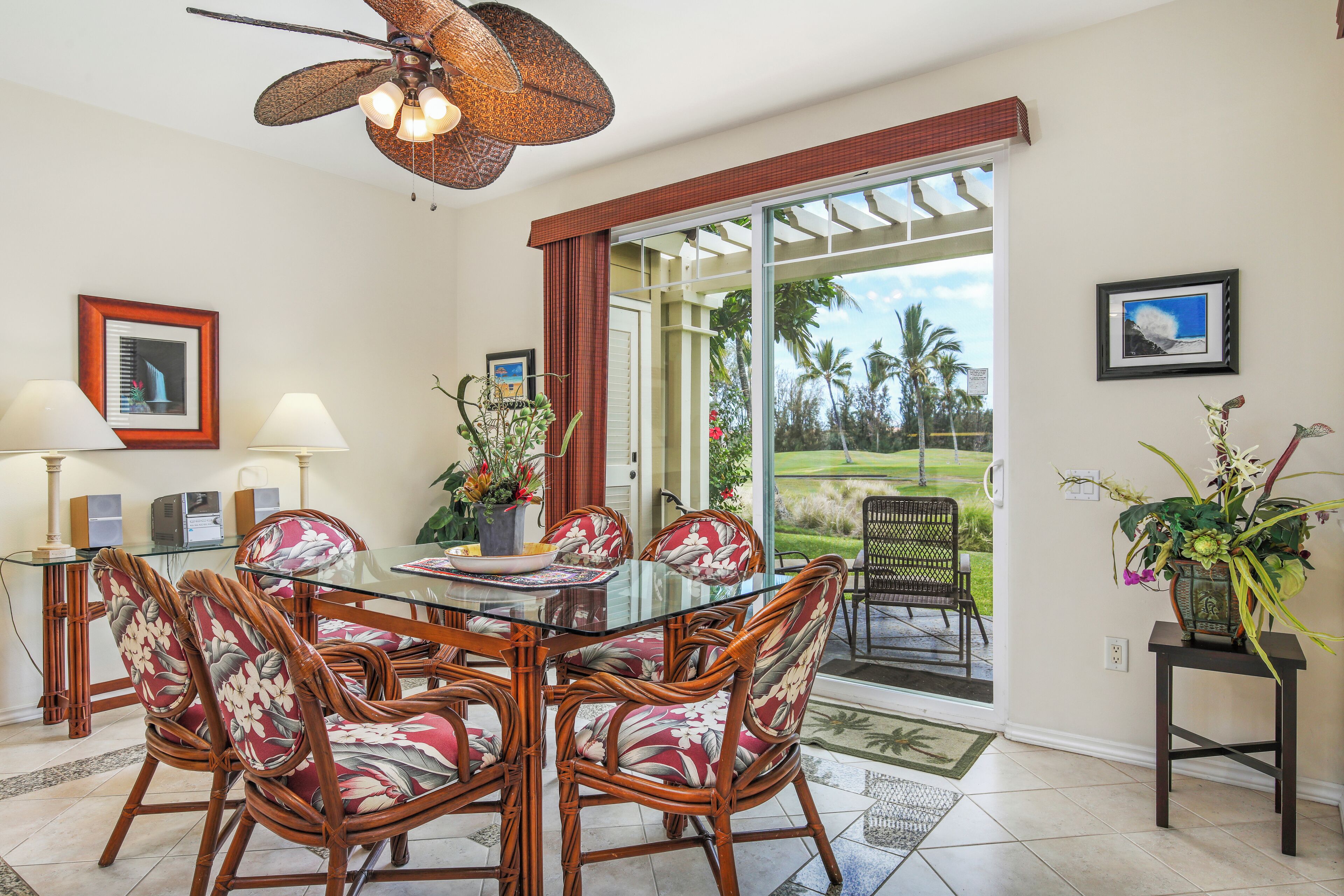 A dining area with a glass table, wicker chairs, and a ceiling fan.