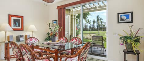 A dining area with a glass table, wicker chairs, and a ceiling fan.
