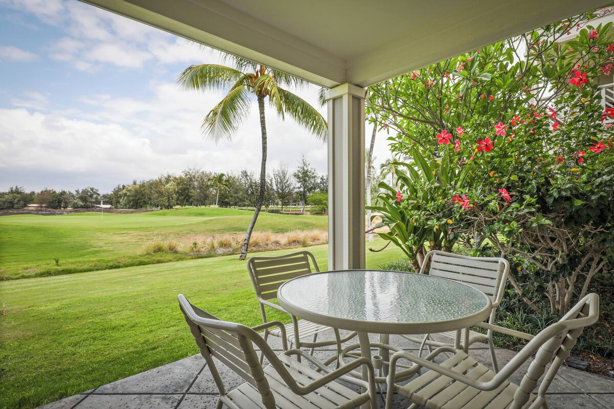 Une terrasse couverte avec une table ronde et des chaises, donnant sur un terrain de golf.