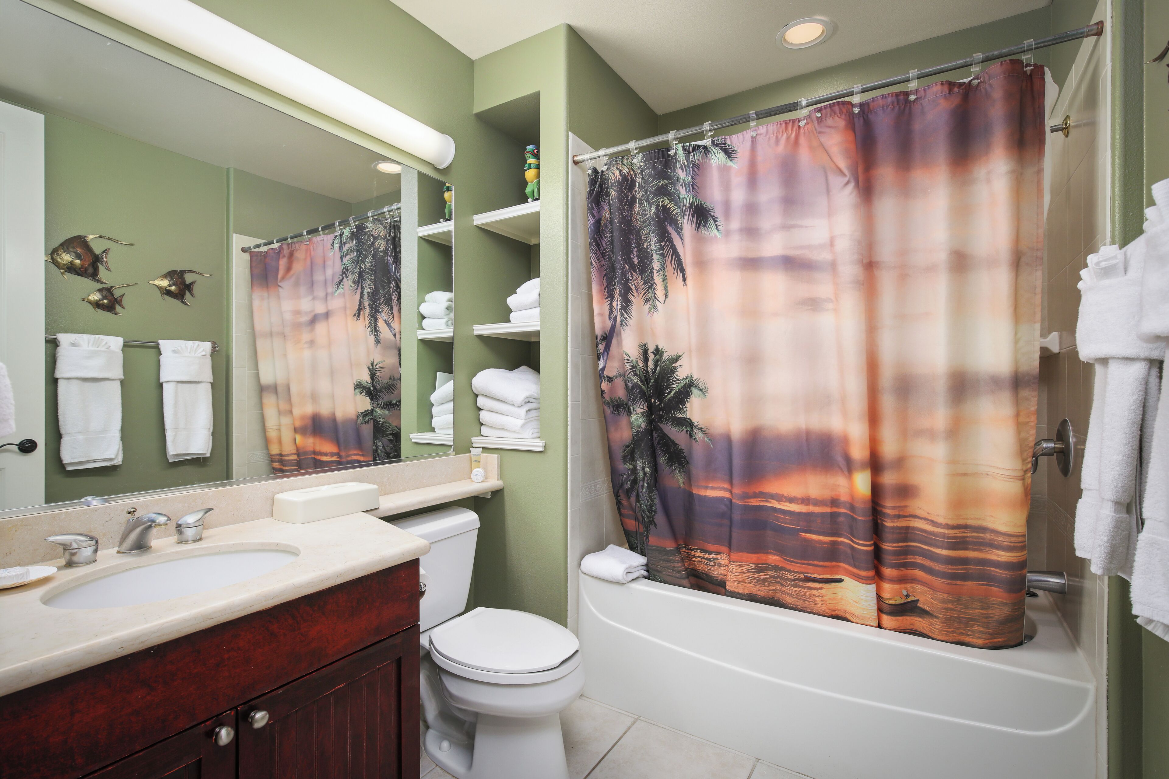 Ein Badezimmer mit weißem Waschbecken, Toilette, Badewanne und einer Duschvorhang mit Sonnenuntergangsmotiv.