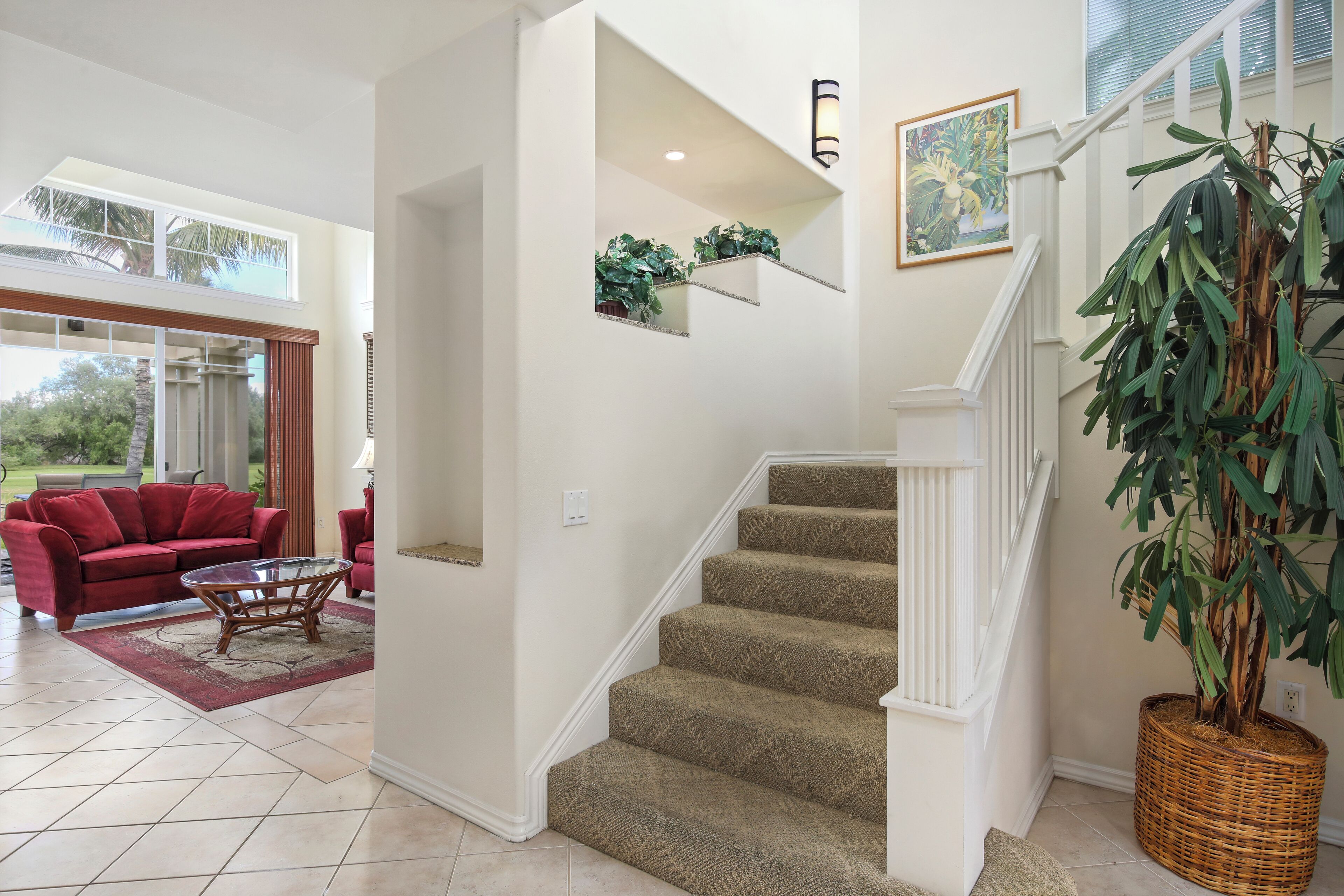 A spacious living area with a red sofa, a glass coffee table, and a staircase with a large plant on the landing.