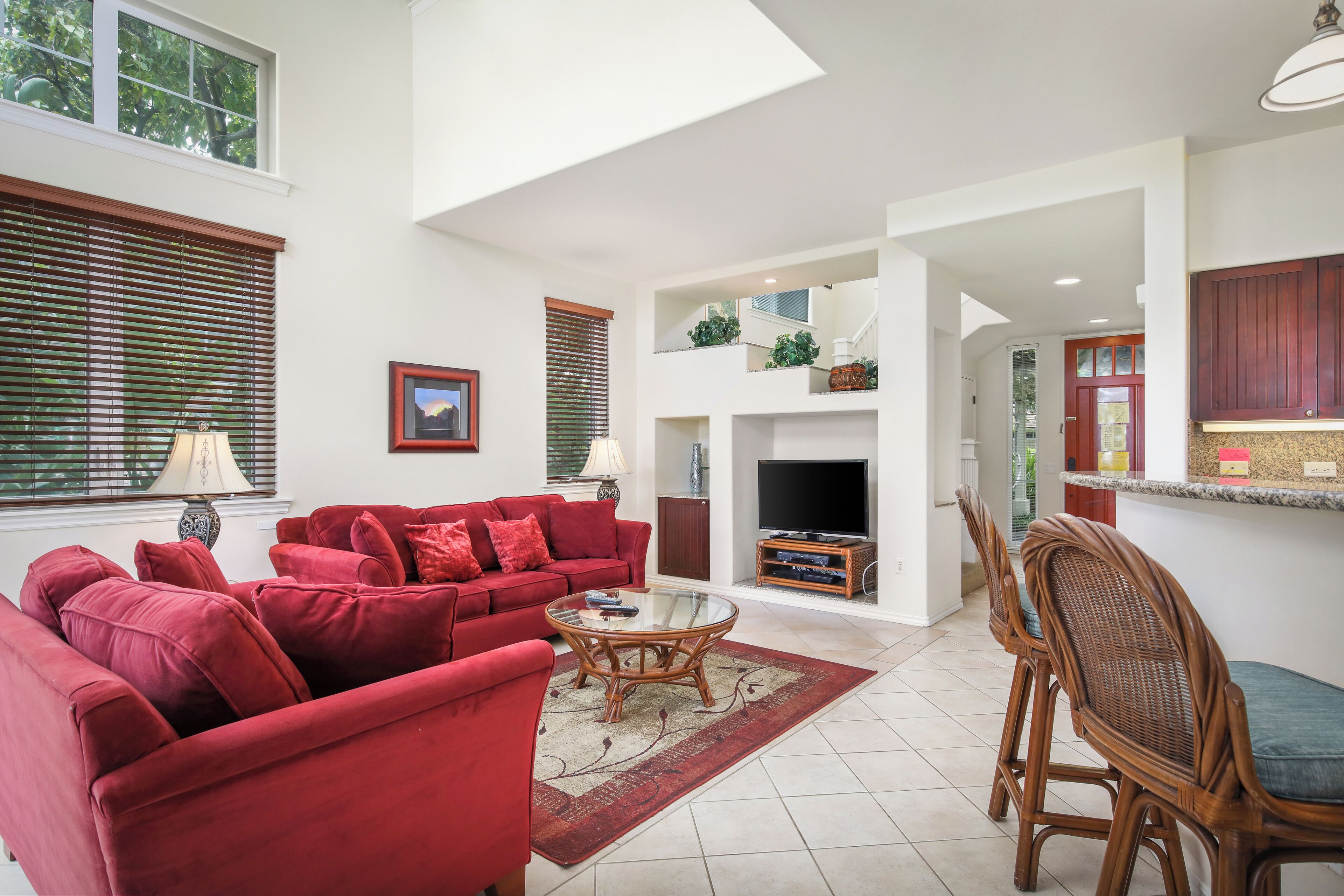 A spacious living area with a red sofa set, a glass coffee table, and a dining area with wicker chairs.