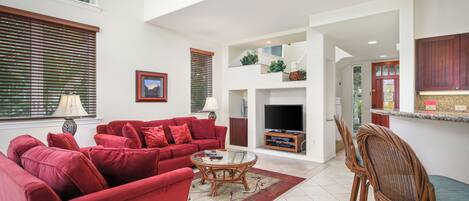 A spacious living area with a red sofa set, a glass coffee table, and a dining area with wicker chairs.