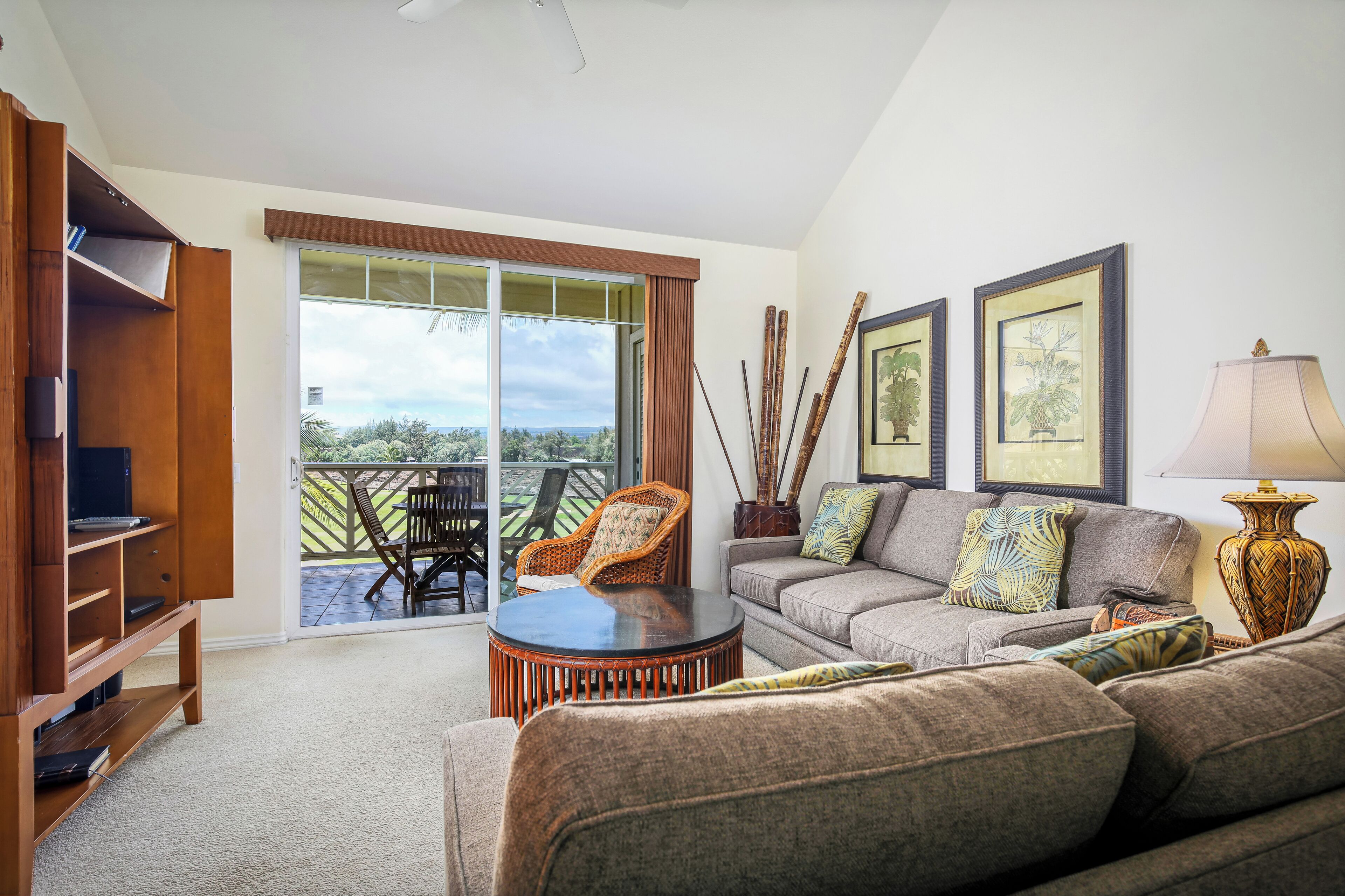 A living room with a sofa, a coffee table, a bookshelf, and a sliding glass door leading to an outdoor patio.