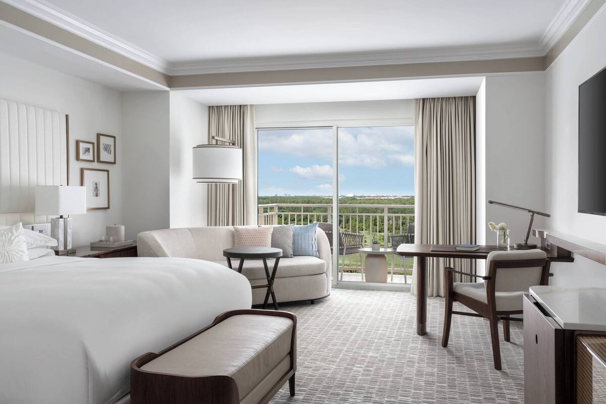 Quarto de hotel com cama grande, sofá, escrivaninha e varanda com vista para a cidade.