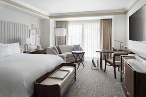 A hotel room with a large bed, a sofa, a desk, and a TV.