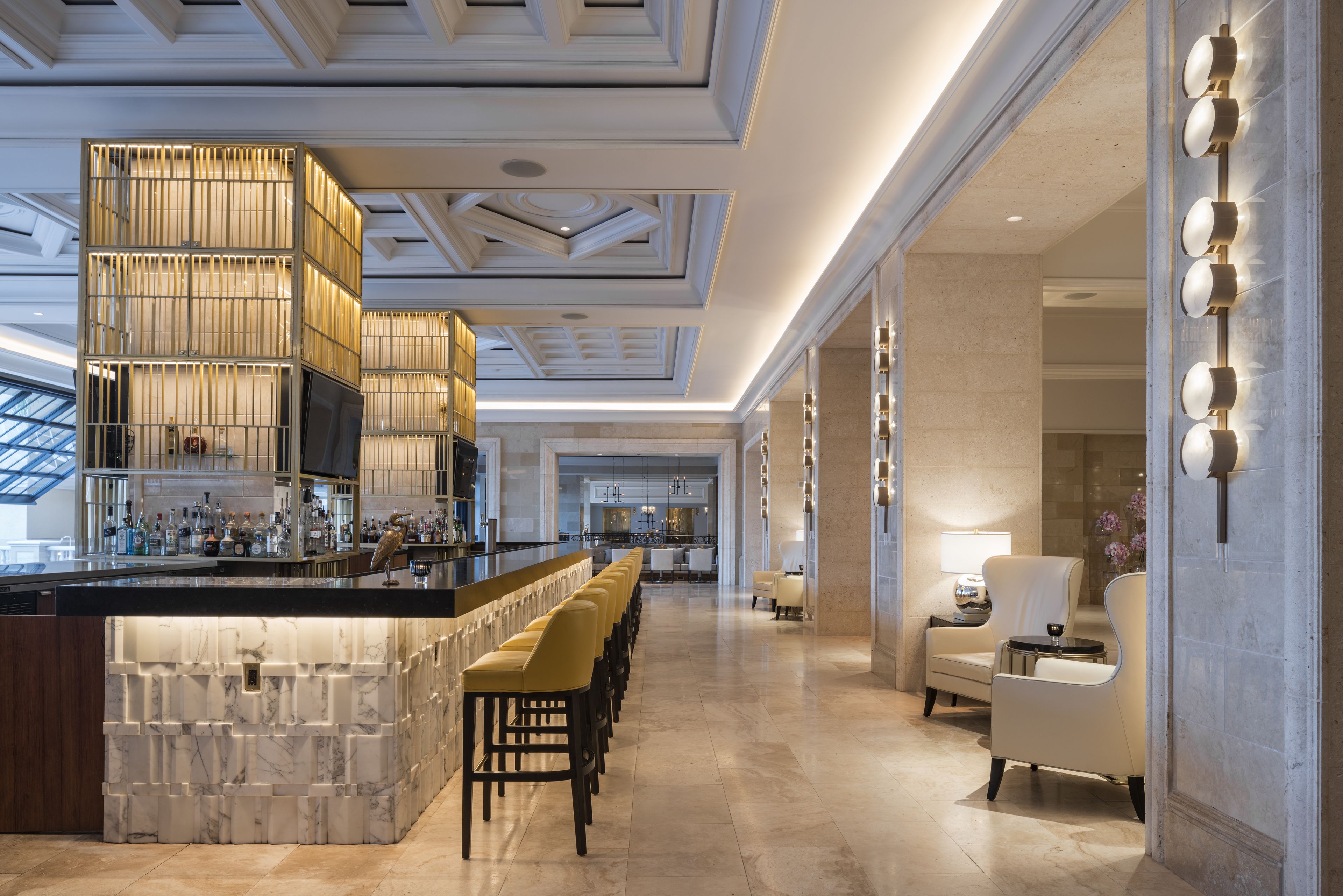 Un moderno bar con barra de mármol, diversas opciones de asiento y un diseño de techo elegante.