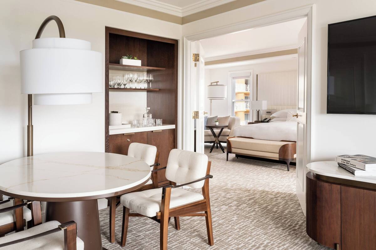 Quarto de hotel com mesa de jantar redonda, sofá, cama e televisão.