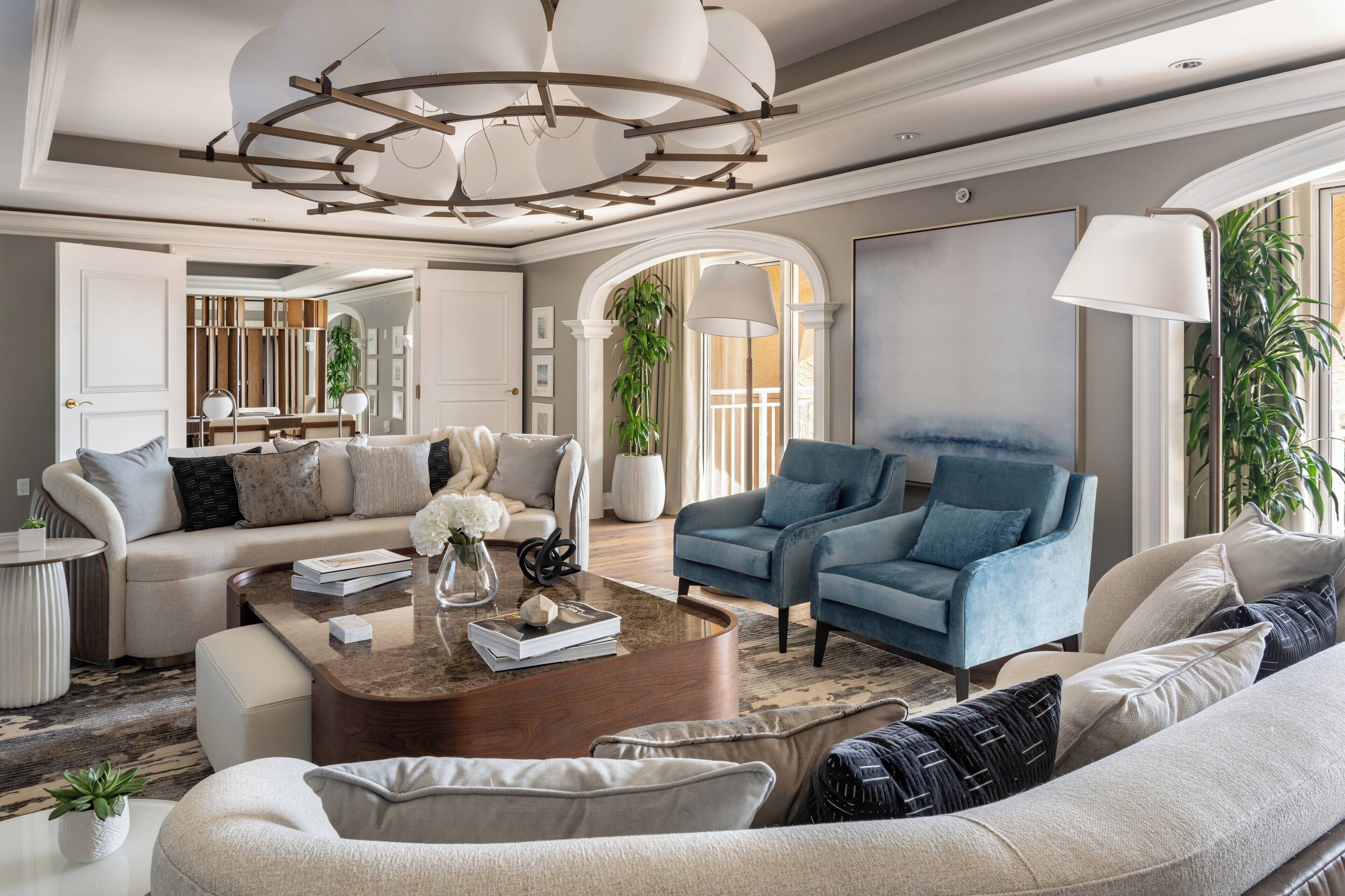 Un salon spacieux agrémenté d’un lustre moderne, d’un fauteuil bleu et d’un canapé beige.