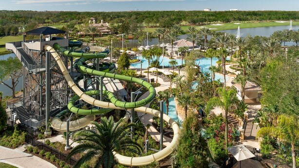 A water park with multiple slides and a pool area surrounded by palm trees and a golf course.