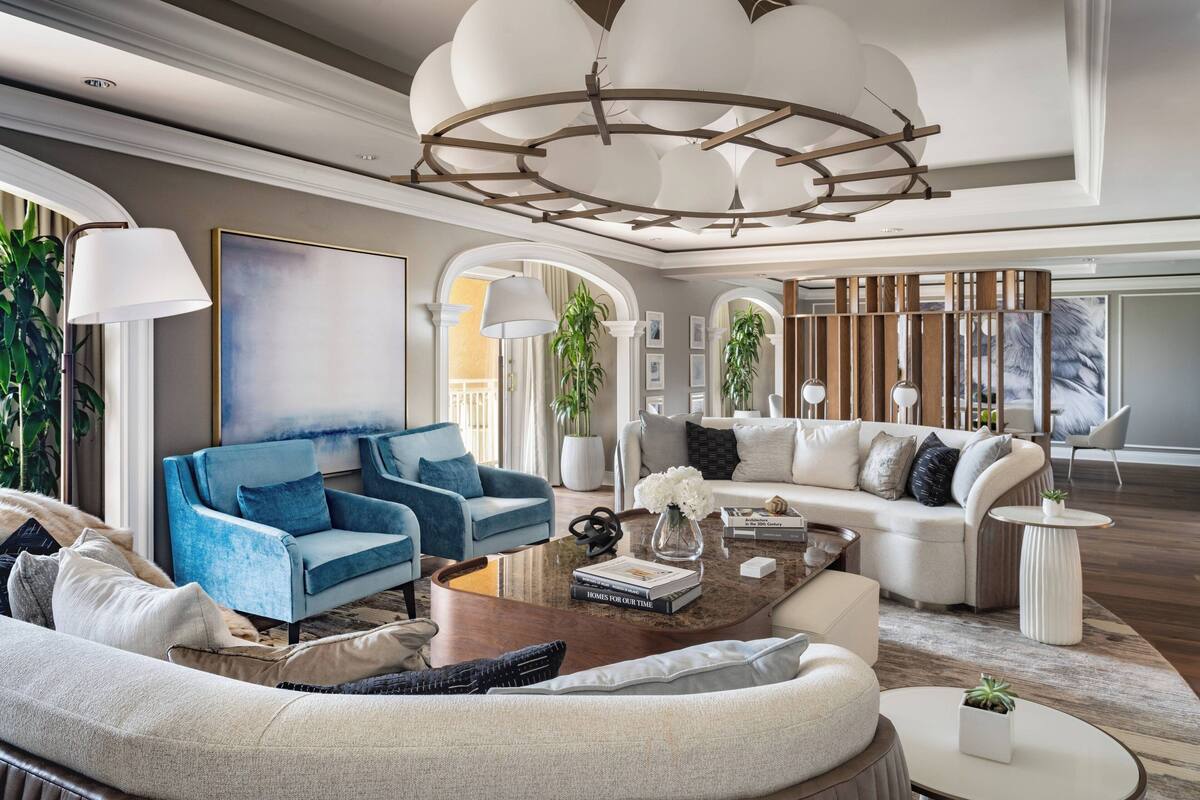 Uma sala de estar espaçosa com um lustre moderno, dois sofás, uma mesa de centro e um quadro grande na parede.