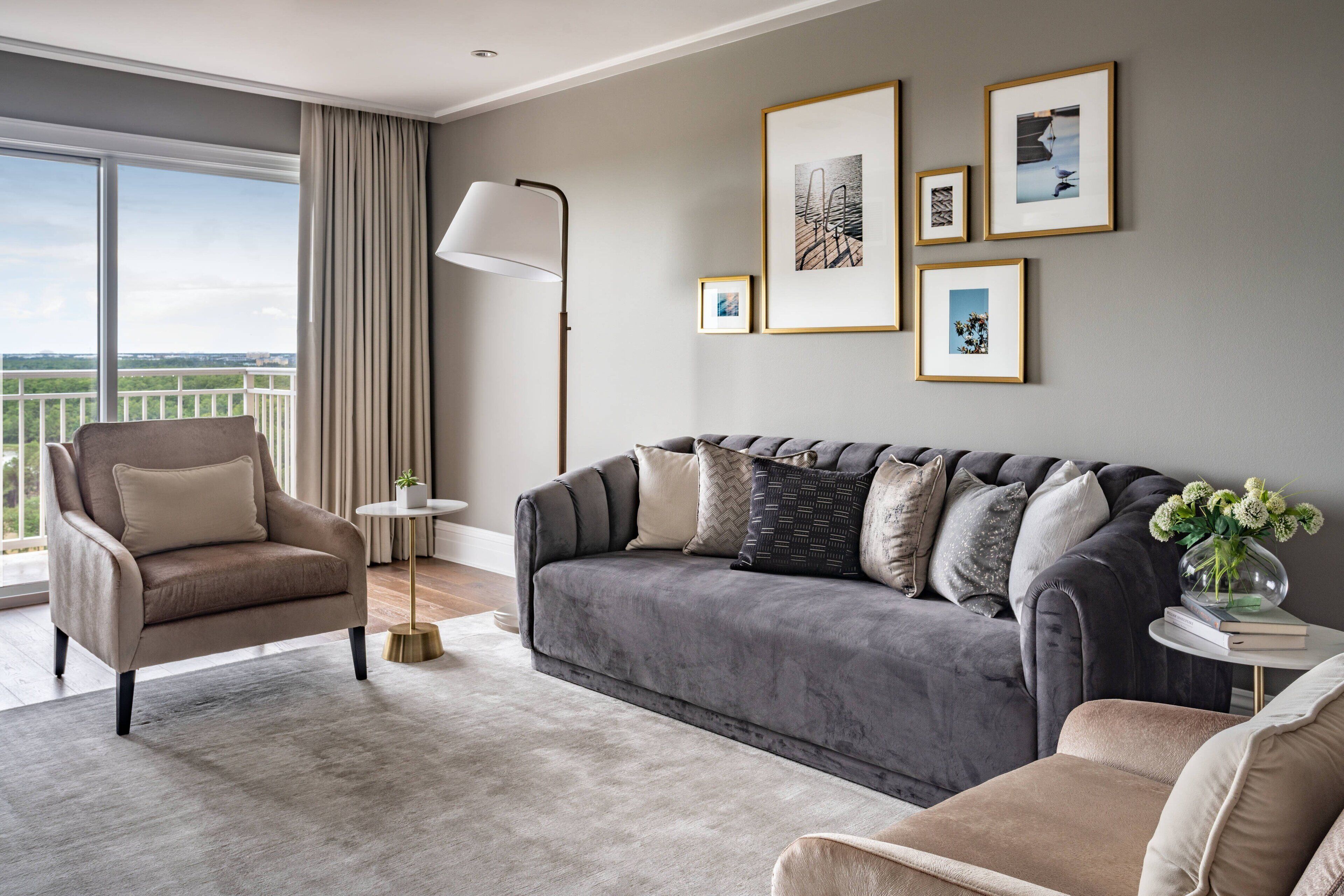 A modern living room with a grey sofa, beige armchair, and a small side table with a vase of flowers.