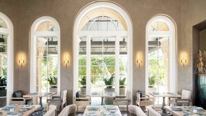 A dining area with tables set for service, large arched windows, and wall-mounted lighting.