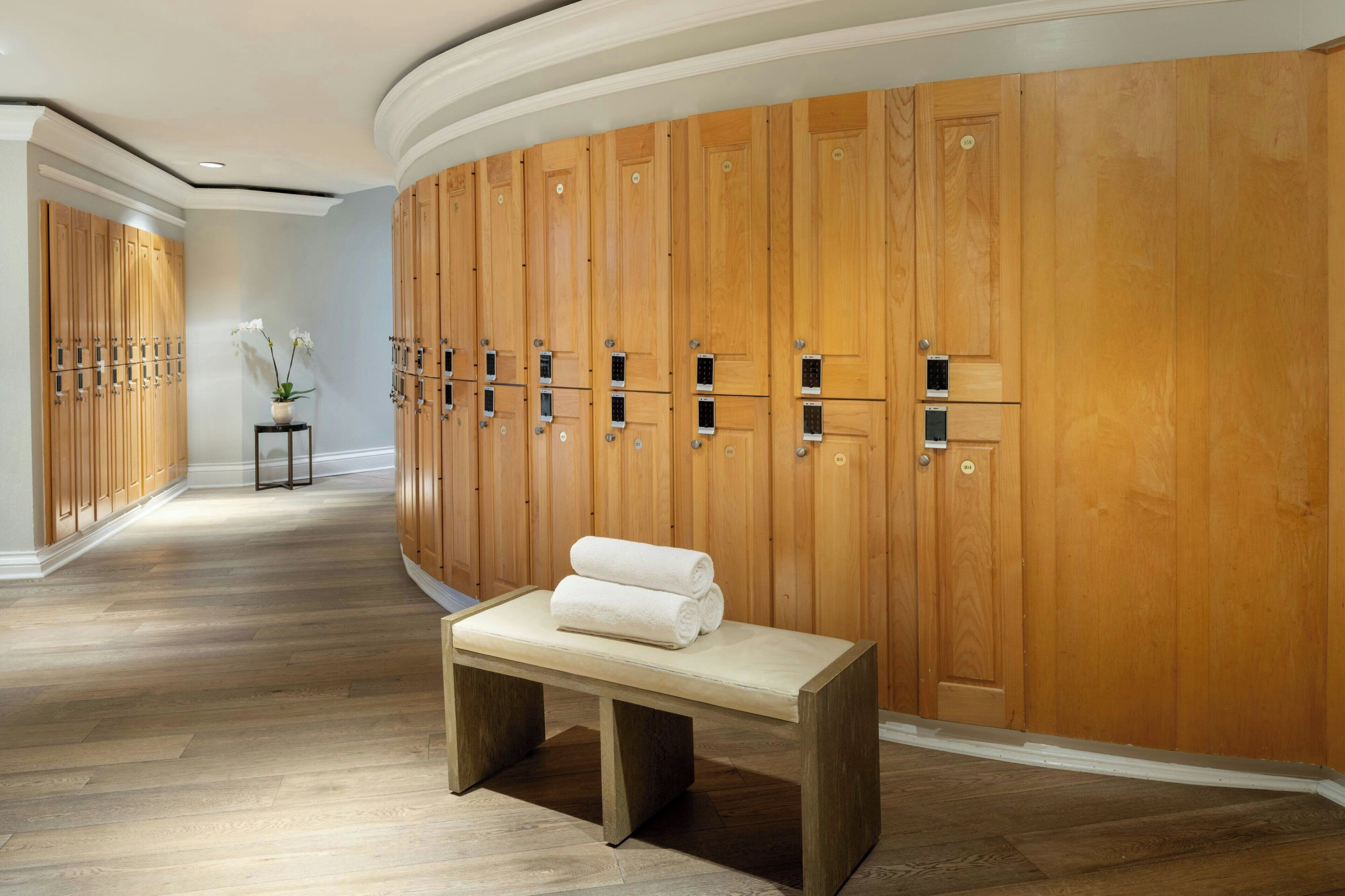 A hotel lobby with wooden lockers, a bench with towels, and a small table with flowers.