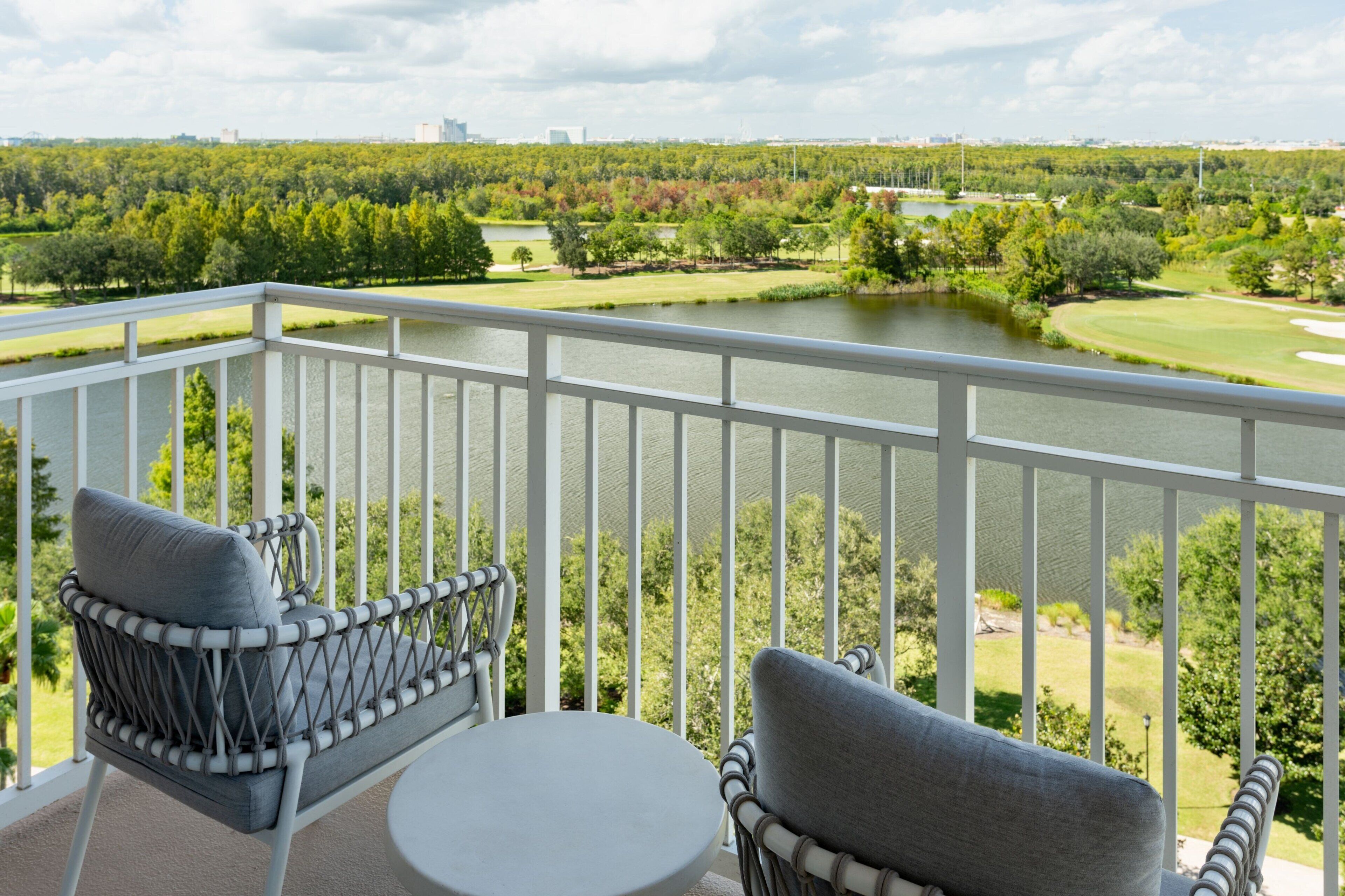 En balkon med fletstole og et lille bord, med udsigt over en golfbane og en sø.